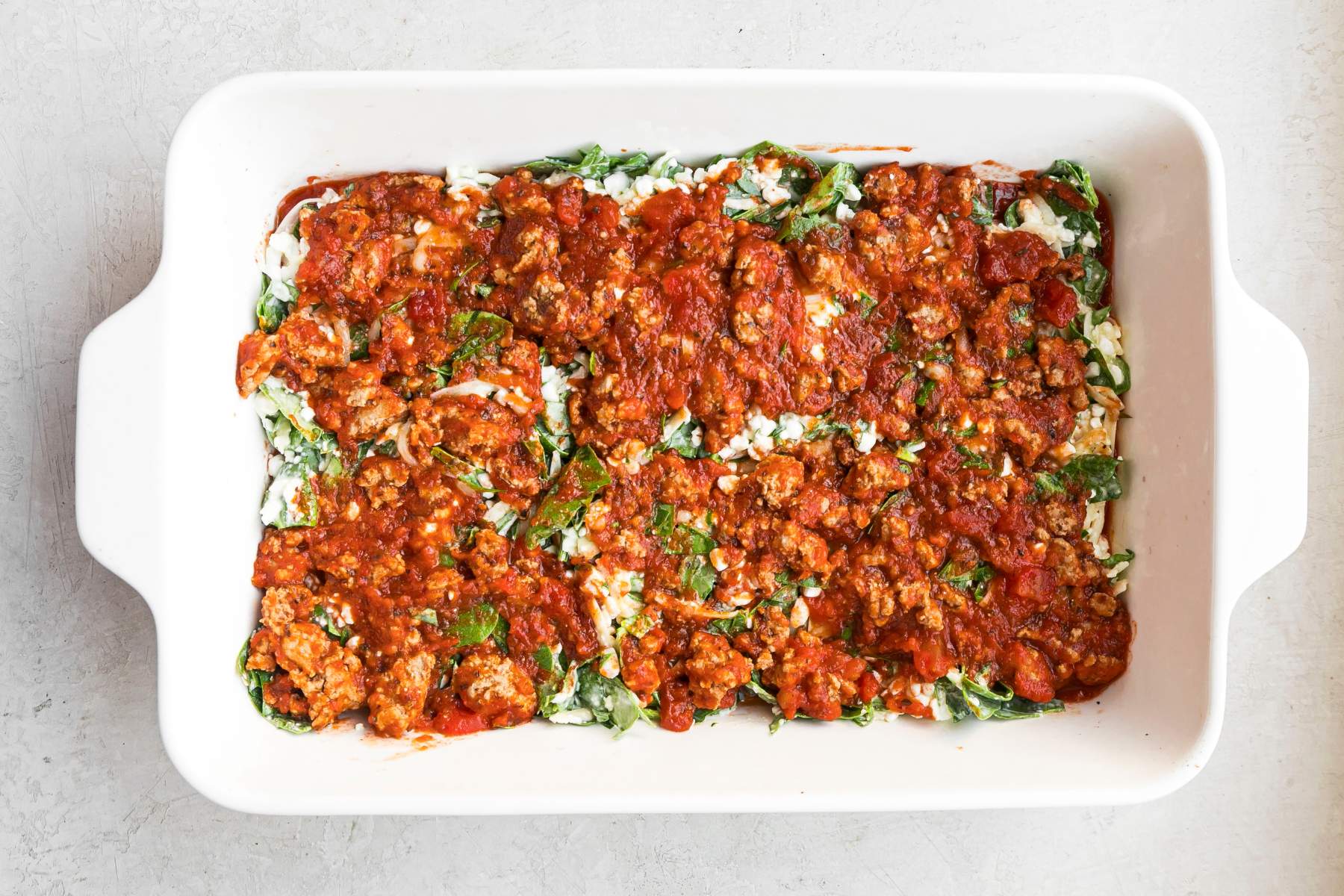 Assembling lasagna with noodles, spinach/cottage cheese mixture and sauce.