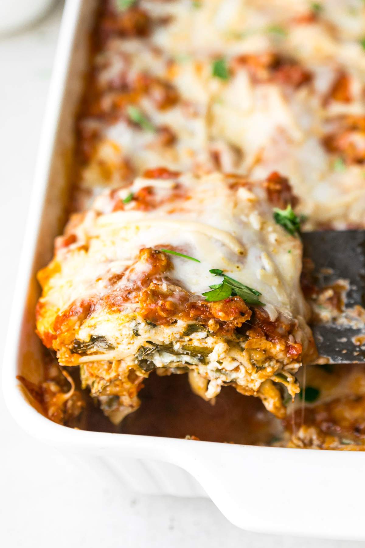Serving a slice of turkey spinach lasagna out of a casserole dish.