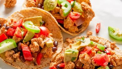 three tacos on a white plate served with lime wedges and jalapeño slices